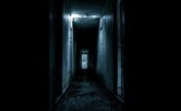 Photograph of a very dark hallway with one sharp light, making it incredibly eerie
