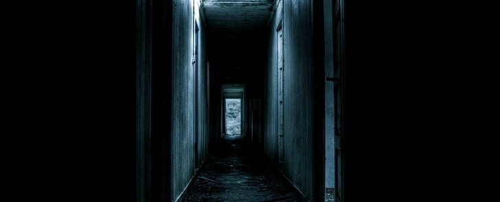 Photograph of a very dark hallway with one sharp light, making it incredibly eerie